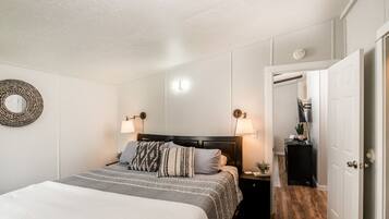 Un dormitorio ordenado con cama, lámparas de noche, un espejo y una puerta que da a otra habitación.