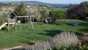 A grassy area with a playground, including swings and a slide, and a view of distant hills and buildings. - Apartment House with garden Tuscany Chianti ,  Florence 15km. (Toscana)