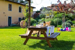 A wooden picnic table set on a grassy lawn with a yellow building in the background.