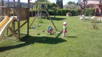 A wooden play structure with a slide and swings in a grassy backyard.