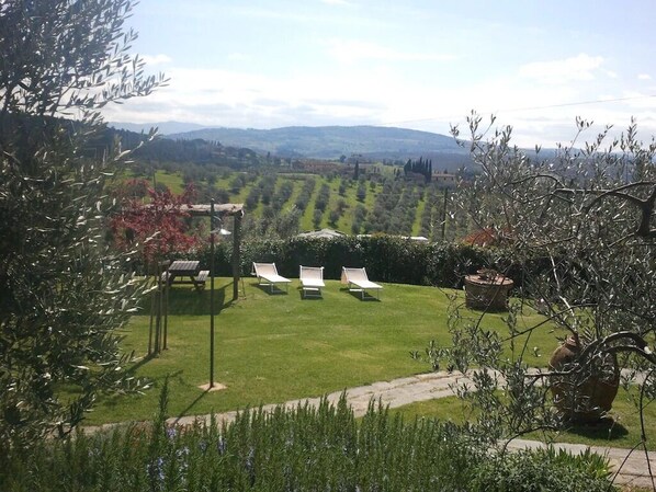A garden with a lawn, three white lounge chairs, and a pergola.