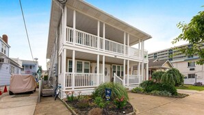 A two-story building with a covered porch and a small garden area. - Beautifully Renovated Beach Block Condo! (Wildwood)