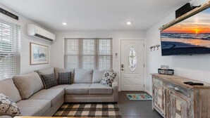 A living room with a sofa, a coffee table, a cabinet, and a wall-mounted TV. - Beautifully Renovated Beach Block Condo! (Wildwood)