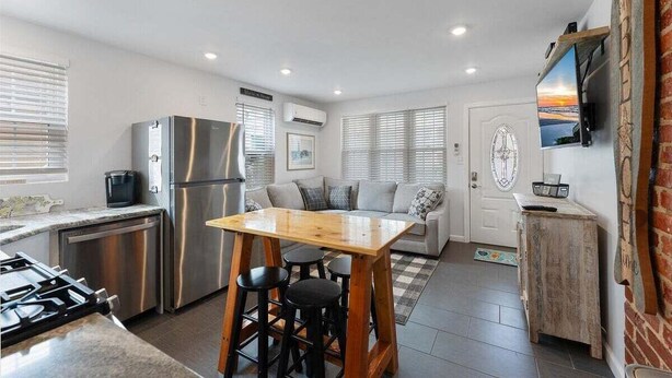 A compact kitchen with a dining area, a refrigerator, a stove, and a television mounted on the wall. - Beautifully Renovated Beach Block Condo! (Wildwood)