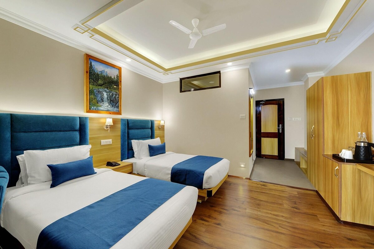 A hotel room with two beds, a ceiling fan, a painting, and a wooden wardrobe.