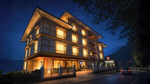 A multi-story hotel with illuminated windows, a signboard, and a view of the road and mountains in the background. - Yashshree Sikkim Blossom 600 Meters From Mg Marg (Gangtok)