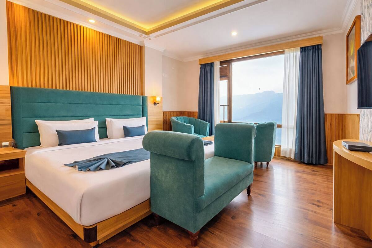 A hotel room with a large bed, two armchairs, a desk, and a TV.