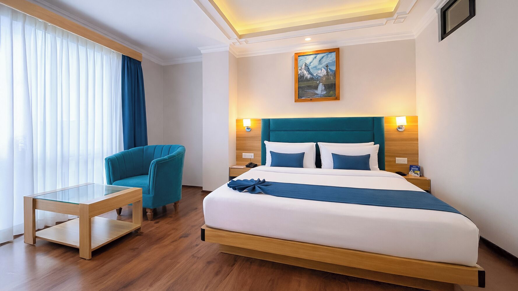 A hotel room with a bed, a chair, a table, and a painting on the wall.