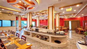 A spacious dining area with multiple tables and chairs, a central counter with kitchenware, and a red accent wall. - Yashshree Sikkim Blossom 600 Meters From Mg Marg (Gangtok)