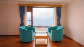 Ein Zimmer mit zwei senffarbenen Sesseln, einem Holztisch und einem großen Fenster mit Vorhängen.