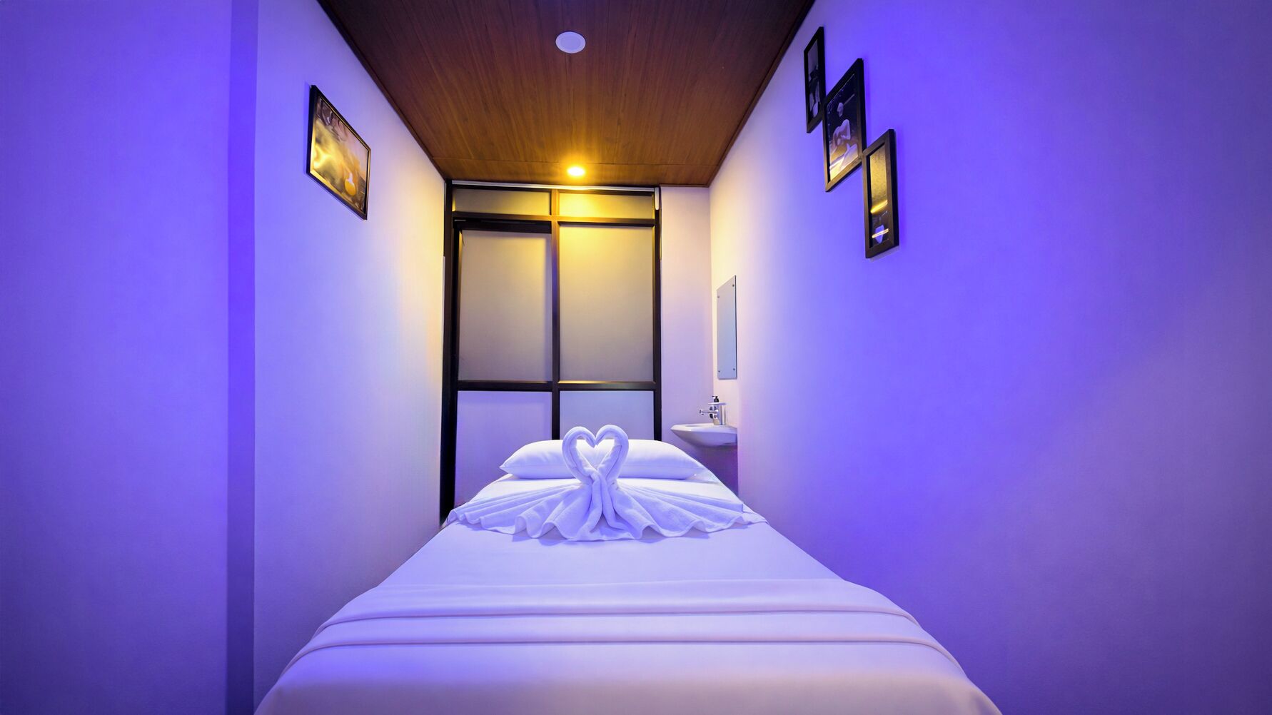 Una habitación de hotel estrecha con cama, mesita de noche, espejo y ventana.