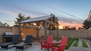 En uteplats med bekväma fåtöljer, en grill och en pergola dekorerad med ljusslingor.