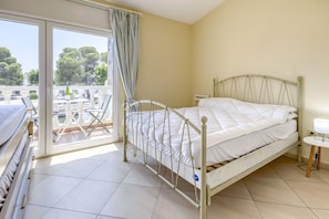 A single-bed room with a metal frame, a white mattress, and a small bedside table with a lamp.