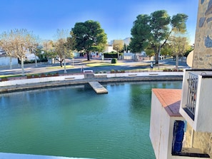 A calm water feature with a stone bridge, surrounded by trees and a paved area with benches.