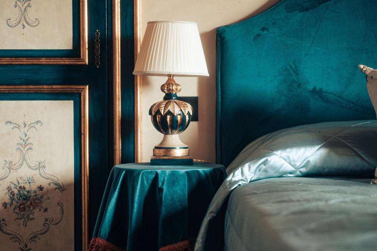A bedroom with a teal headboard, a bedside table with a lamp, and a bed with a grey duvet.