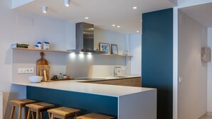 A modern kitchen with a large island, wooden stools, and built-in shelves.