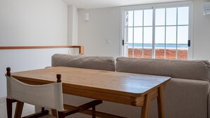 A dining area with a wooden table and chairs, a cushioned bench, and a large window with a view of the sea.