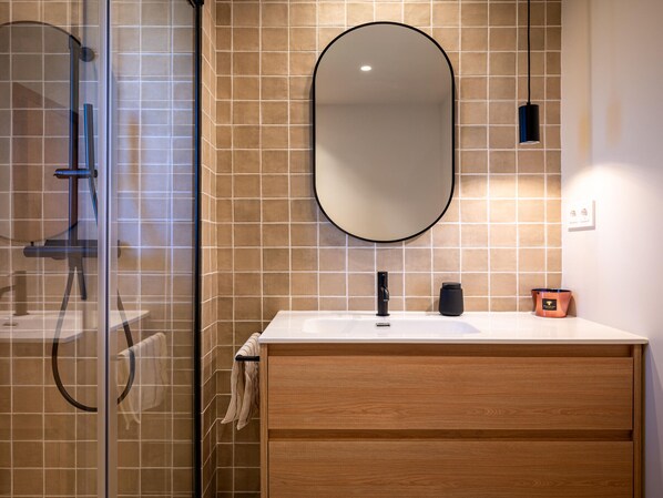 A modern bathroom with a glass shower enclosure, a wooden vanity with a sink, and a large mirror.