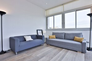 Un salon moderne avec deux canapés gris, une lampe sur pied et une grande fenêtre donnant sur la ville.