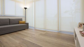 Una sala de estar moderna con un sofá, una lámpara de pie y ventanas amplias.