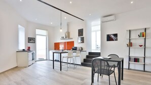 Una cocina moderna con armarios blancos, un comedor con mesa y sillas, y una estantería con libros y objetos decorativos.