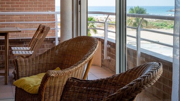 A balcony with wicker furniture, a view of the beach, and a brick wall. - Seafront apartment with pool and parking in Torredembarra (Torredembarra)