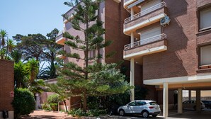 A multi-story building with a brick facade, balconies, and a parking area with cars. - Seafront apartment with pool and parking in Torredembarra (Torredembarra)