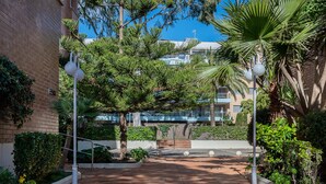 A paved walkway with a brick pattern, surrounded by lush greenery and palm trees. - Seafront apartment with pool and parking in Torredembarra (Torredembarra)