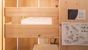 A wooden bunk bed with a white mattress, a wooden wall with a map and a plaque, and a small wooden shelf.