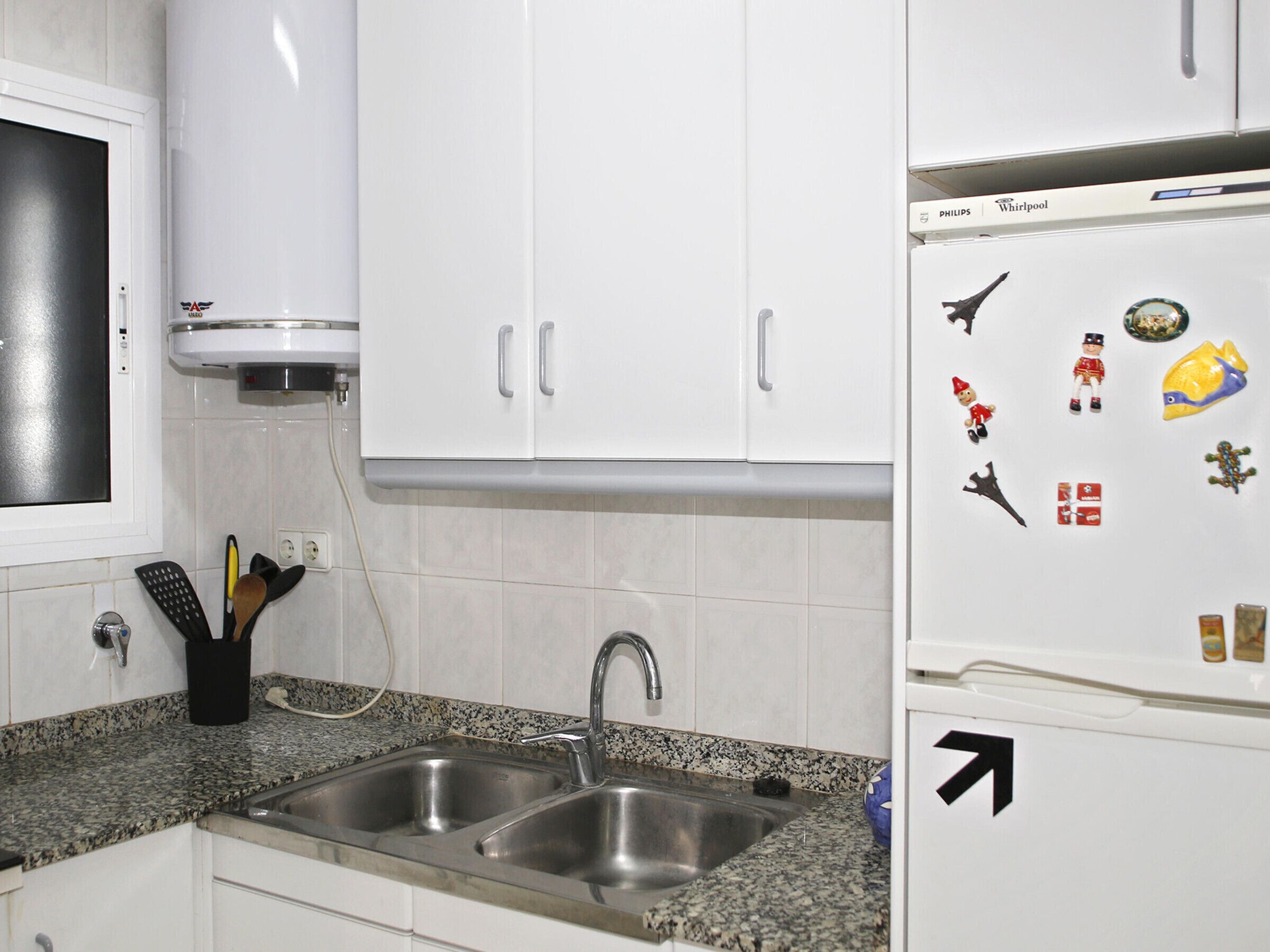 A kitchen with white cabinets, a double sink, and a refrigerator with magnets.