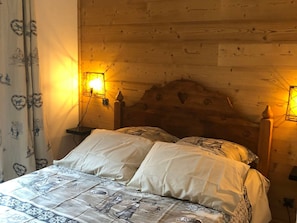 Uma cama de madeira com colcha acolchoada, duas luminárias de cabeceira e uma cortina estampada.