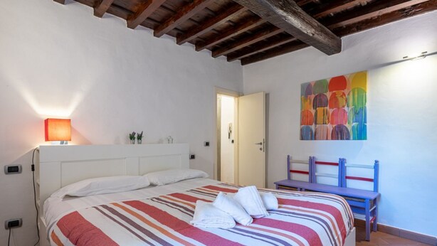 Une chambre à coucher avec un lit, une table de chevet, une chaise, un tableau et une porte.