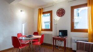 Une pièce comprenant une table à manger, des chaises rouges, une horloge, un téléviseur et un radiateur.