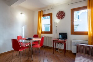 Une pièce comprenant une table à manger, des chaises rouges, une horloge, un téléviseur et un radiateur.