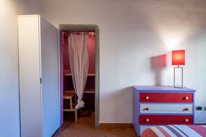 A bedroom with a wardrobe, a bedside table with a lamp, and a bed with a striped blanket. - GuestHost - Cozy and colorful apartment of about 40 sqm, ideal for 2 people, located on the second floor of an ancient and characteristic building (NO lift). The property is located in the historic center of Florence (Restricted-Traffic Area), in the liv (Florence)