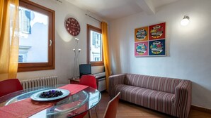 A room with a glass dining table, red chairs, a striped sofa, a clock, and a poster on the wall. - GuestHost - Cozy and colorful apartment of about 40 sqm, ideal for 2 people, located on the second floor of an ancient and characteristic building (NO lift). The property is located in the historic center of Florence (Restricted-Traffic Area), in the liv (Florence)