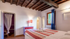Une chambre à coucher comprenant un lit, une table de chevet, une lampe, une fenêtre avec des rideaux, une porte et une armoire.