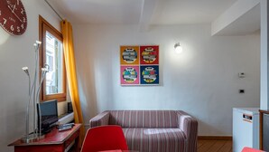 A living room with a striped sofa, a glass table, a red chair, a TV, a clock, and a refrigerator. - GuestHost - Cozy and colorful apartment of about 40 sqm, ideal for 2 people, located on the second floor of an ancient and characteristic building (NO lift). The property is located in the historic center of Florence (Restricted-Traffic Area), in the liv (Florence)