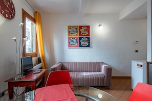 Een woonkamer met een gestreepte bank, een glazen tafel, een rode stoel, een televisie, een klok en een koelkast.