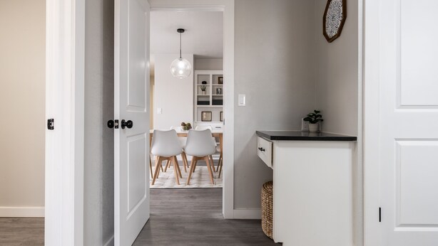 Un couloir avec un coin repas Ă lâarriĂšre, comprenant une porte blanche, un petit comptoir de cuisine et un luminaire suspendu.