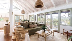 Amplia sala de estar con un sofá verde grande, muebles de mimbre y vistas al exterior a través de ventanas grandes.