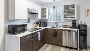 A modern kitchen with white cabinets, a stainless steel dishwasher, a coffee maker, and a microwave. - ★Serene & Stylish by the Lake | ♛QueenBed, FirePit (Talkeetna)