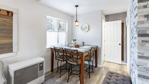 A dining area with a wooden table and chairs, a hanging light fixture, and a stone wall. - ★Serene & Stylish by the Lake | ♛QueenBed, FirePit (Talkeetna)