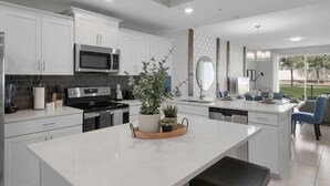 A modern kitchen with white cabinetry, a central island, a microwave, and a dining area with a view.