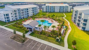 A modern apartment complex with a central swimming pool surrounded by lounge chairs and palm trees.
