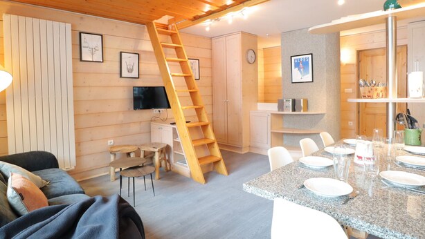 A cozy room with a wooden ceiling, a dining area with a granite table, and a TV mounted on the wall. - Comfortable apartment for 6 with balcony and parking in Les Gets (Les Gets)