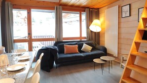 A cozy living room with a dark sofa, a dining table set for two, and a wooden bookshelf. - Comfortable apartment for 6 with balcony and parking in Les Gets (Les Gets)