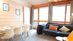 A cozy room with a dining table set for four, a sofa with cushions, and large windows with curtains. - Comfortable apartment for 6 with balcony and parking in Les Gets (Les Gets)