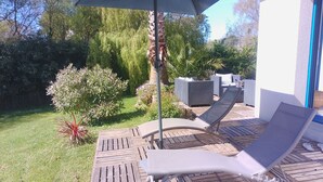 Eine Terrasse mit zwei Liegestühlen, einem Tisch und einem großen Sonnenschirm.
