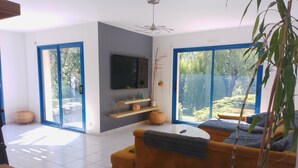Ein modernes Wohnzimmer mit einer Couch, einem Fernseher und bodentiefen Glasschüben, die zu einem Garten führen.